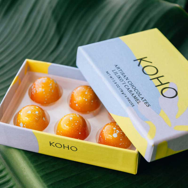 Open box of KOHO Lilikoi Caramel 6-piece assortment on a tropical leaf